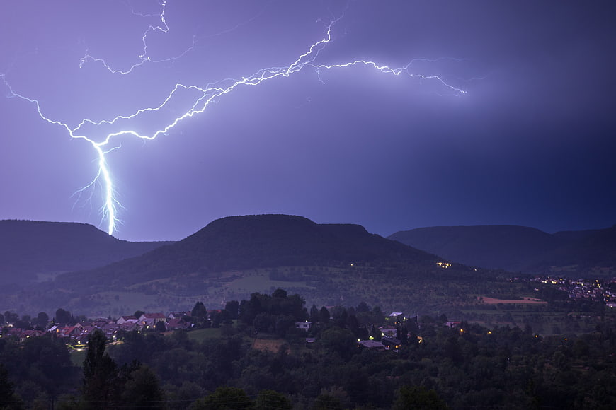 Dramatic Lightning Strike Over Mountainous Landscape at Night