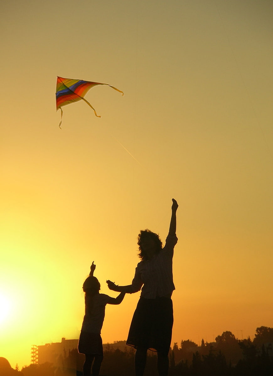 Silhouette of Mother and Child Flying Kite at Sunset