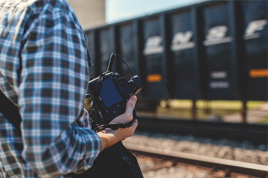 Photographer holding DSLR camera near train tracks