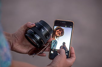 Hands holding camera lens and smartphone displaying selfie