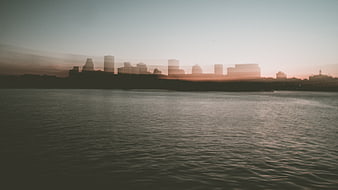 Hazy City Skyline Silhouette Over Calm Water at Sunset