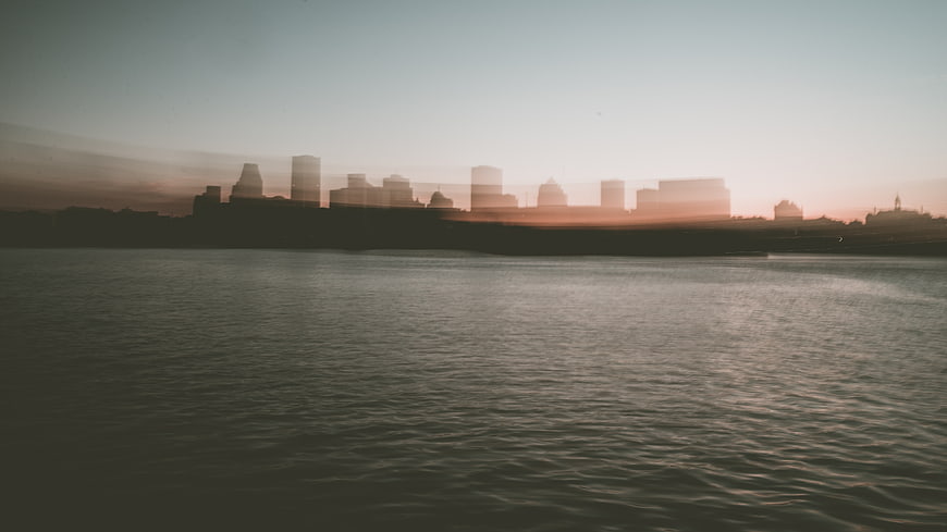 Hazy City Skyline Silhouette Over Calm Water at Sunset