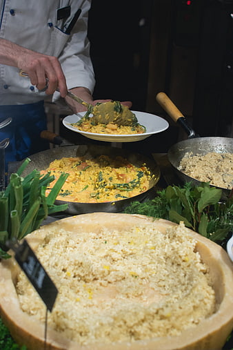 Chef serving creamy risotto from a large cheese wheel