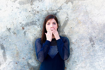 Young woman covering mouth in surprise against textured concrete wall
