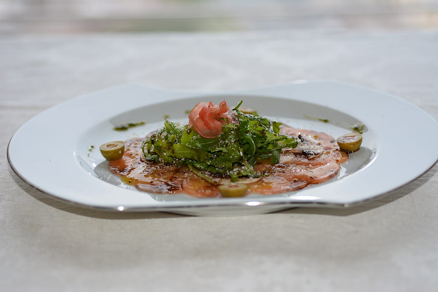 Gourmet Carpaccio with Arugula and Olives on White Plate