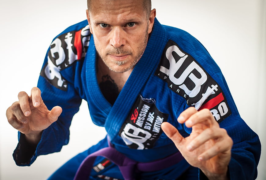 Intense male BJJ fighter in blue gi with purple belt