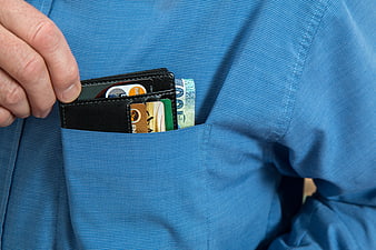 Close-up of hand holding wallet with cash and cards in blue shirt pocket