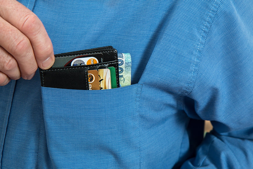 Close-up of hand holding wallet with cash and cards in blue shirt pocket