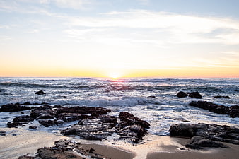 Sunset over rocky ocean coastline with waves crashing on sand