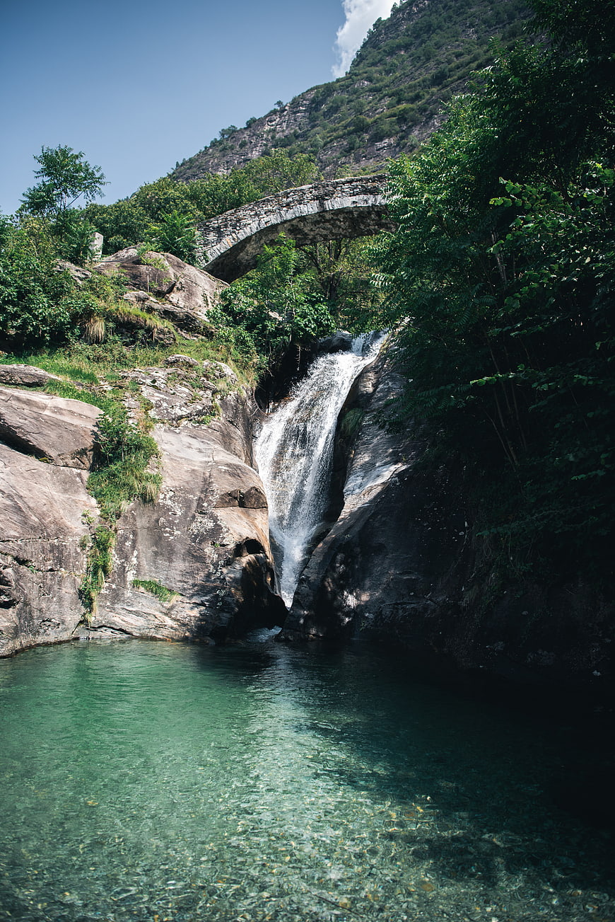 Scenic waterfall cascading into a clear pool beneath an ancient stone bridge