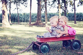 Two happy children hugging in a red wagon outdoors