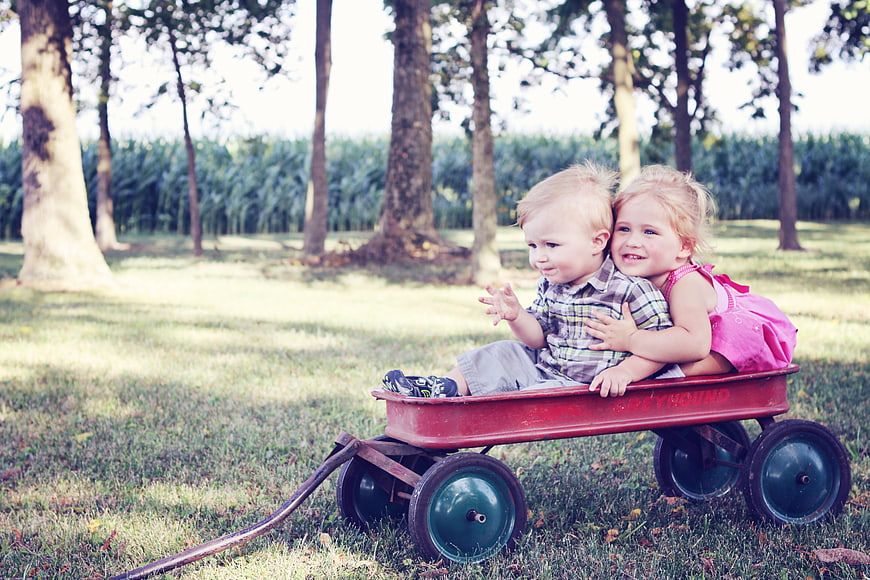 Two happy children hugging in a red wagon outdoors