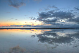 Serene sunset reflection on calm ocean water with clouds