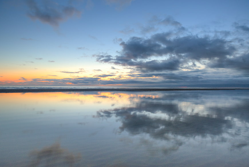 Serene sunset reflection on calm ocean water with clouds