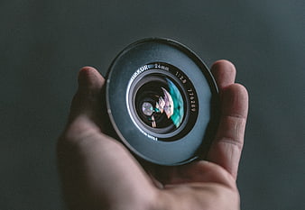Hand holding vintage camera lens against dark background
