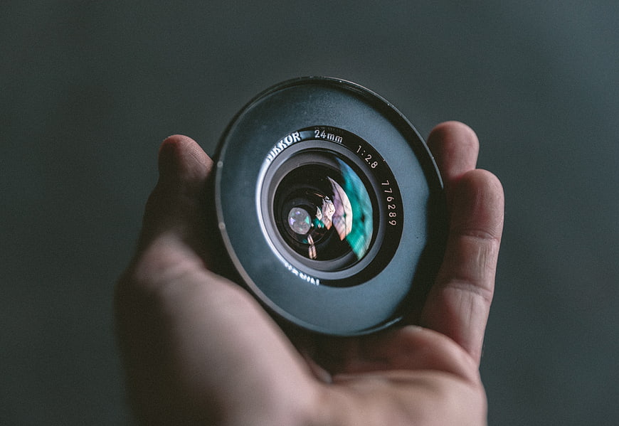 Hand holding vintage camera lens against dark background