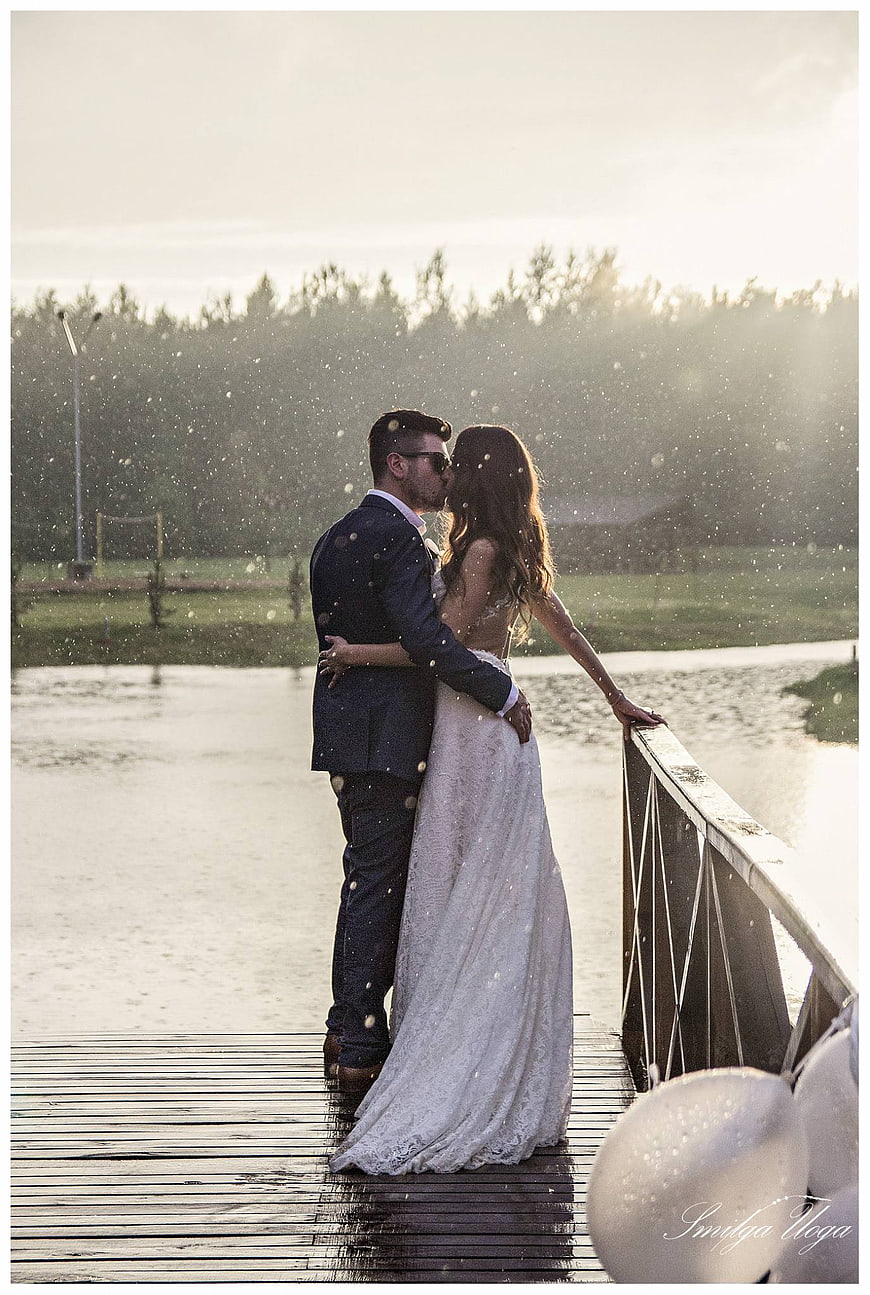 Romantic Wedding Couple Kissing in Rain on Wooden Pier