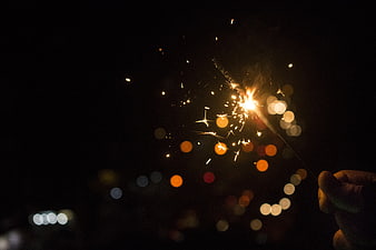 Hand holding sparkler with bokeh lights against dark night background