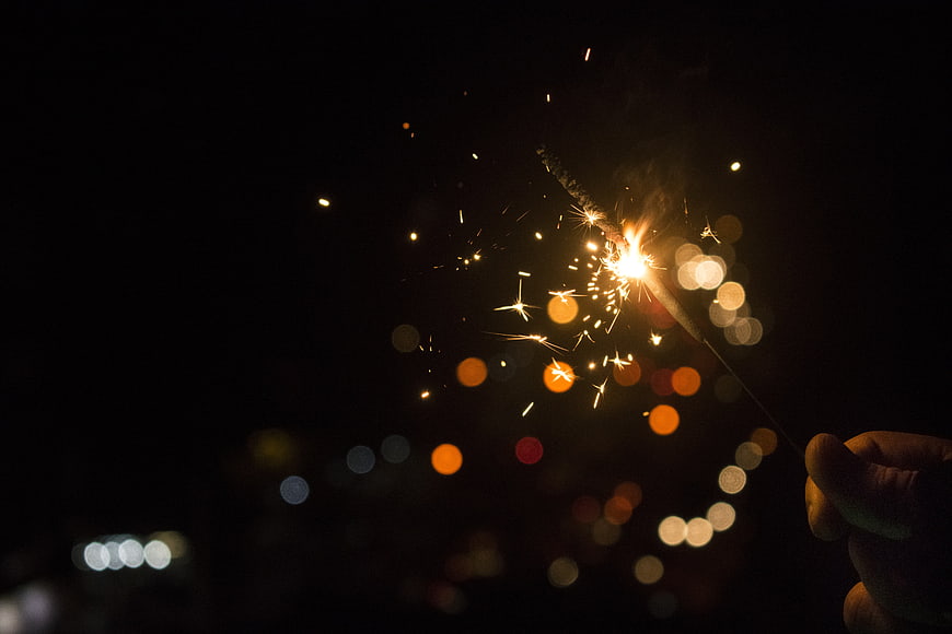 Hand holding sparkler with bokeh lights against dark night background