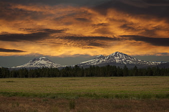 Dramatic sunset over snow-capped mountains and grassy meadow