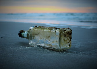 Weathered glass bottle lying on dark sand at the ocean shoreline during sunset