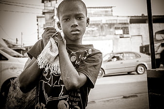 Portrait of a young African boy holding a woven sack on a street