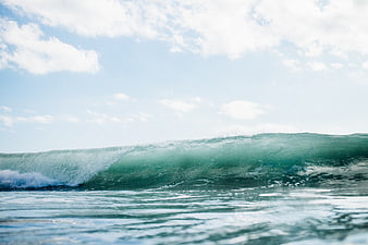 Cinematic ocean wave curling under blue sky with clouds