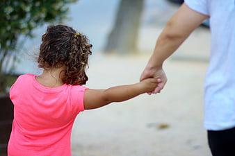 Child holding adult hand outdoors walking