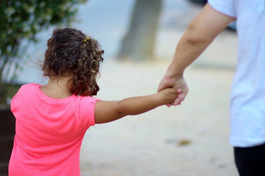 Child holding adult hand outdoors walking
