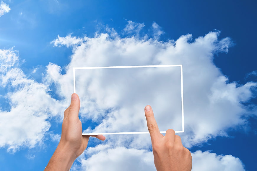 Hands holding transparent tablet frame against blue sky clouds