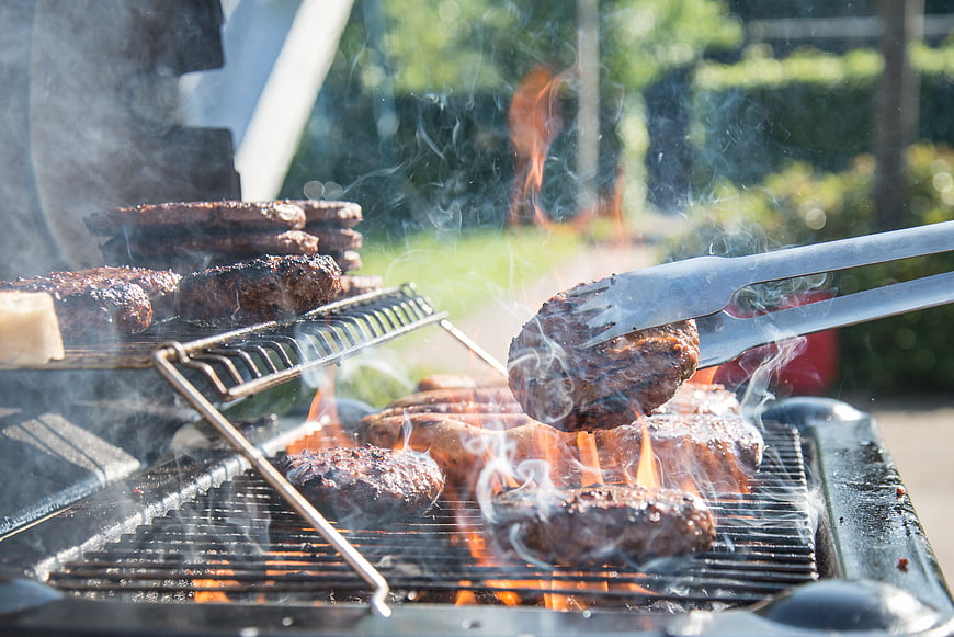 Grilling juicy burger patties on outdoor barbecue with tongs