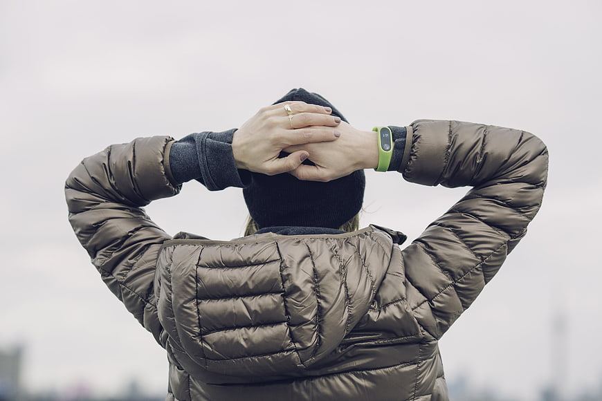 Woman in puffer jacket adjusting beanie with fitness tracker
