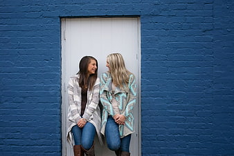 Two happy young women laughing in front of a blue brick wall