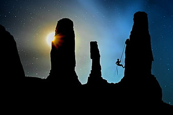 Silhouette of Rock Climber Rappelling Between Rock Formations at Night