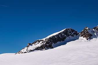 Snowy mountain peak with small building against blue sky