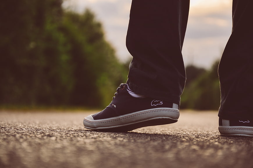 Close-up of black sneakers on asphalt road at sunset