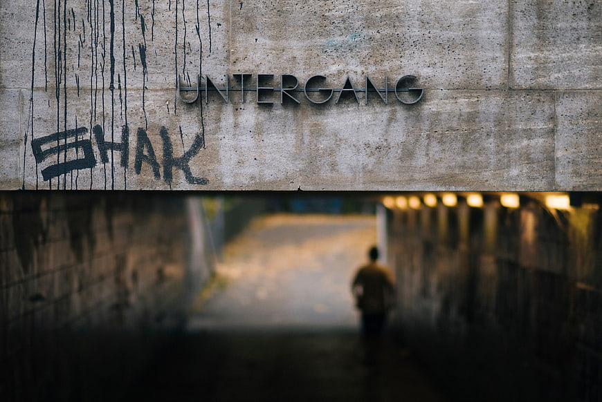Man walking away in concrete tunnel with Untergang sign
