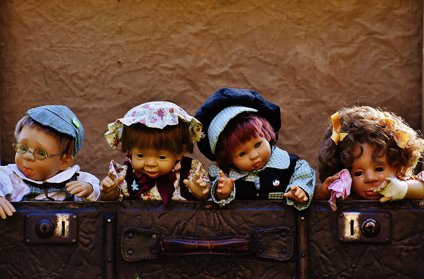 Vintage dolls peeking over antique leather suitcase