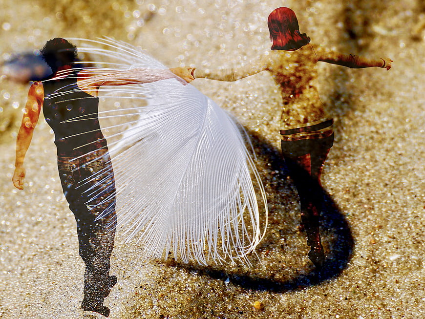 Couple holding hands with giant white feather on sand
