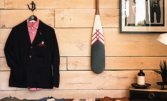 Men's navy blazer and pink shirt hanging on wooden wall with oar