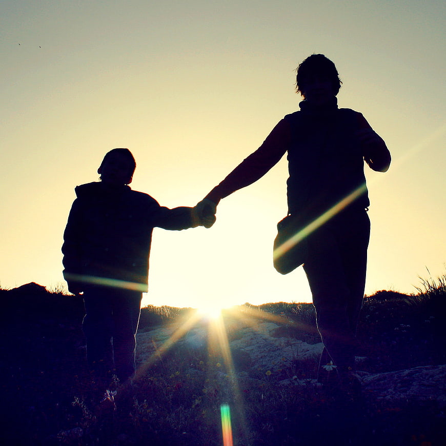 Silhouette of mother and child holding hands at sunset