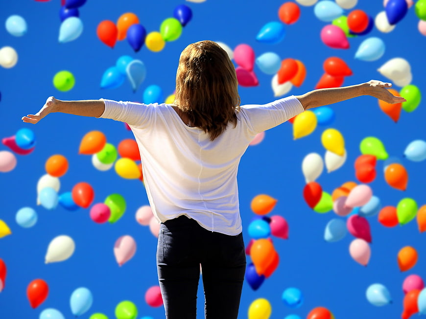 Woman with arms outstretched releasing colorful balloons into blue sky