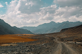 Dirt road winding through mountain valley with dramatic clouds