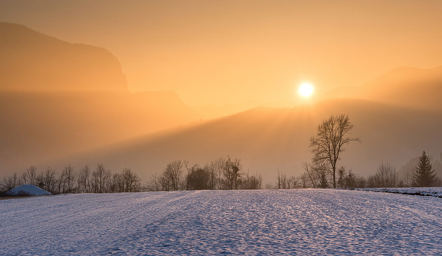 Golden sunrise over snowy winter mountain landscape with trees