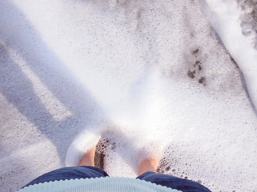 Bare feet in foamy ocean waves on sandy beach