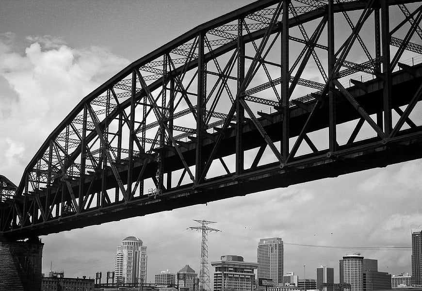 Black and white steel truss bridge over city skyline