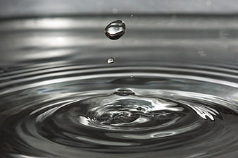 Macro water droplet splash with ripples on dark surface
