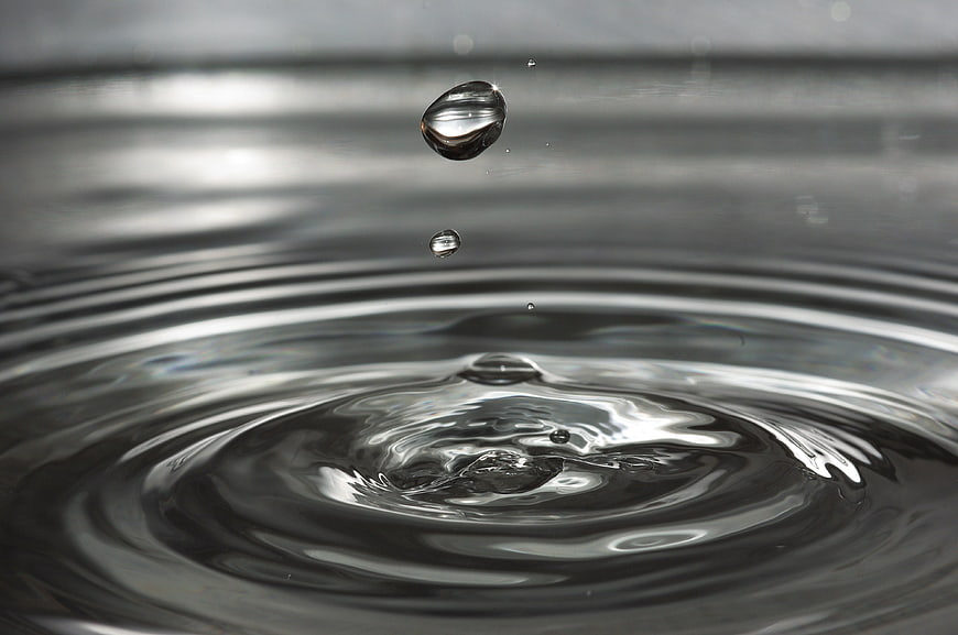 Macro water droplet splash with ripples on dark surface