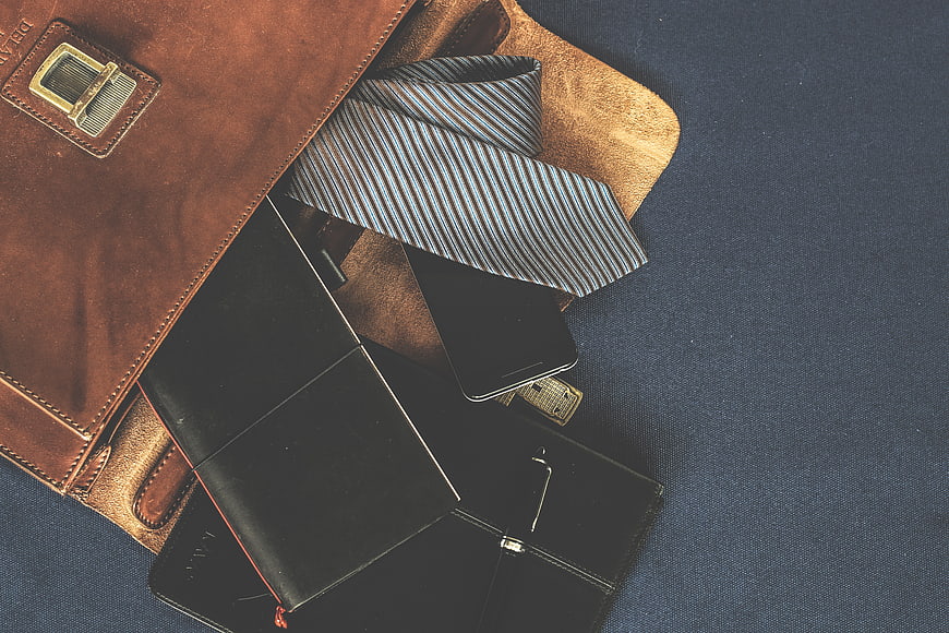 Leather satchel with tie, wallet, and smartphone on blue background