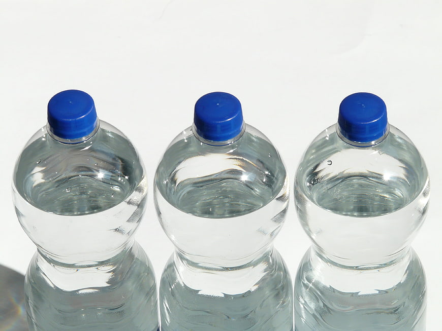 Three Clear Plastic Water Bottles with Blue Caps on White Background